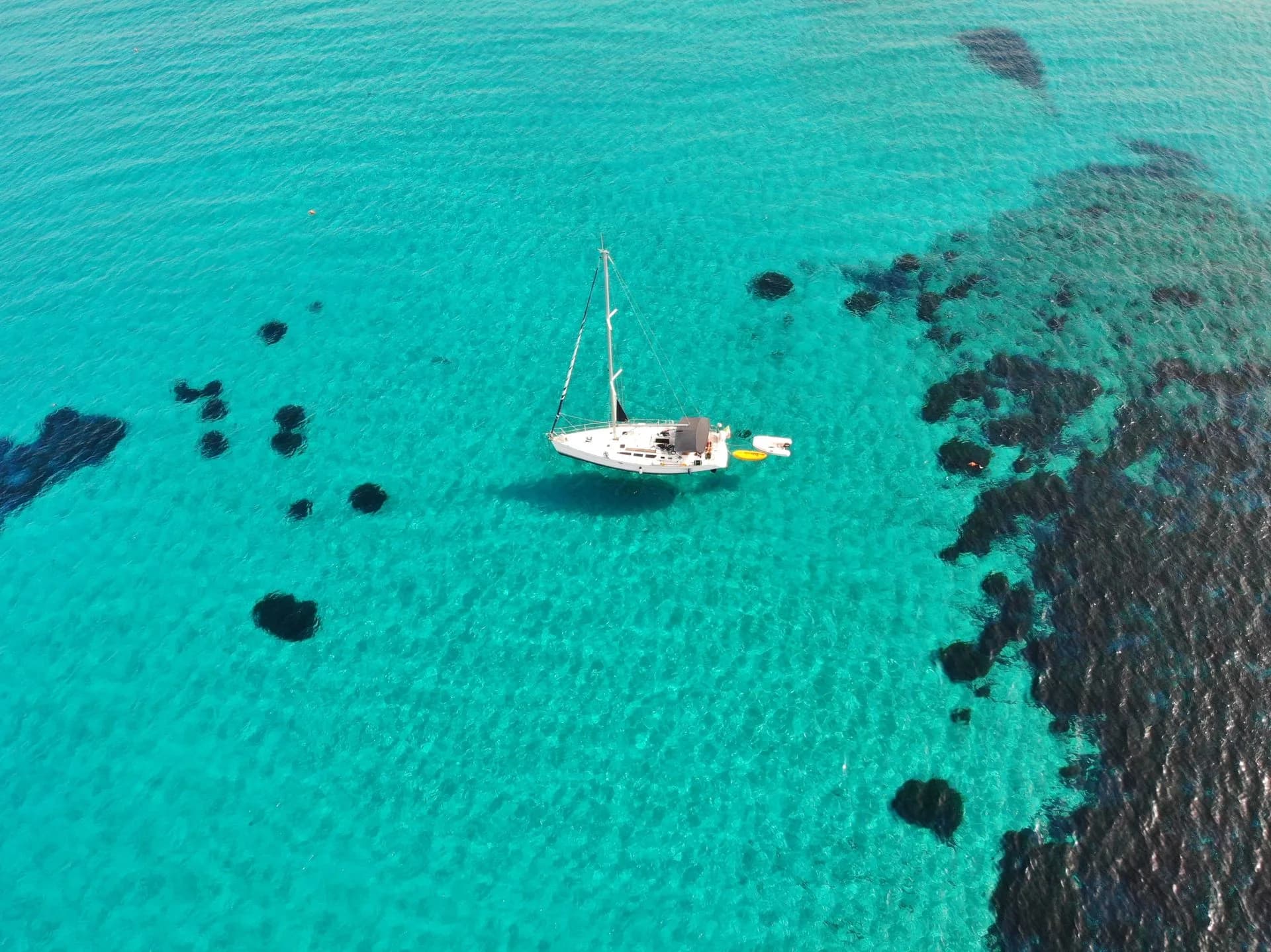 Aerial view of a sailboat in clear turquoise water near Geremeas, Sardinia