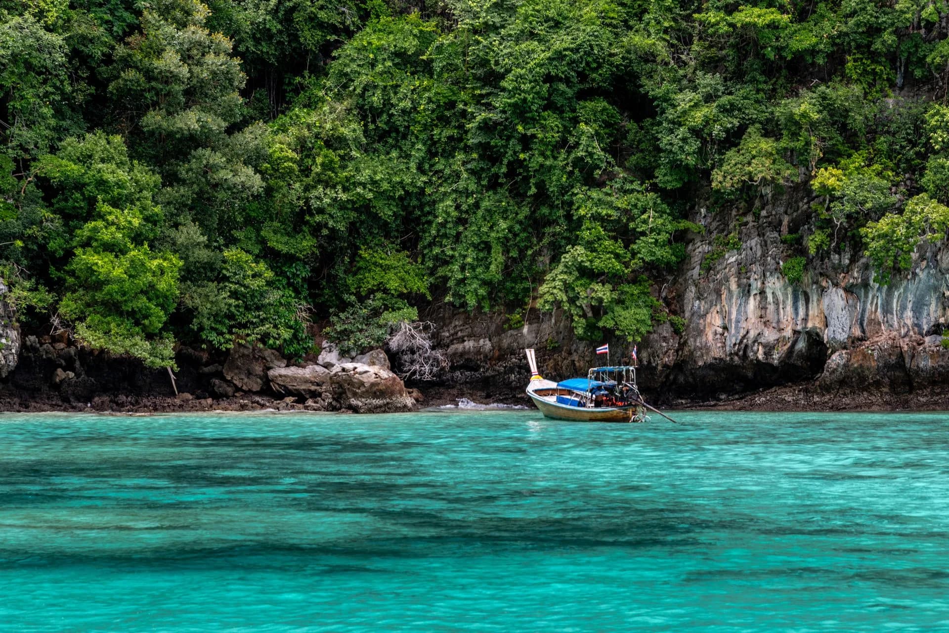 Traditional boat beside lush coastal cliffs in Phuket, Thailand