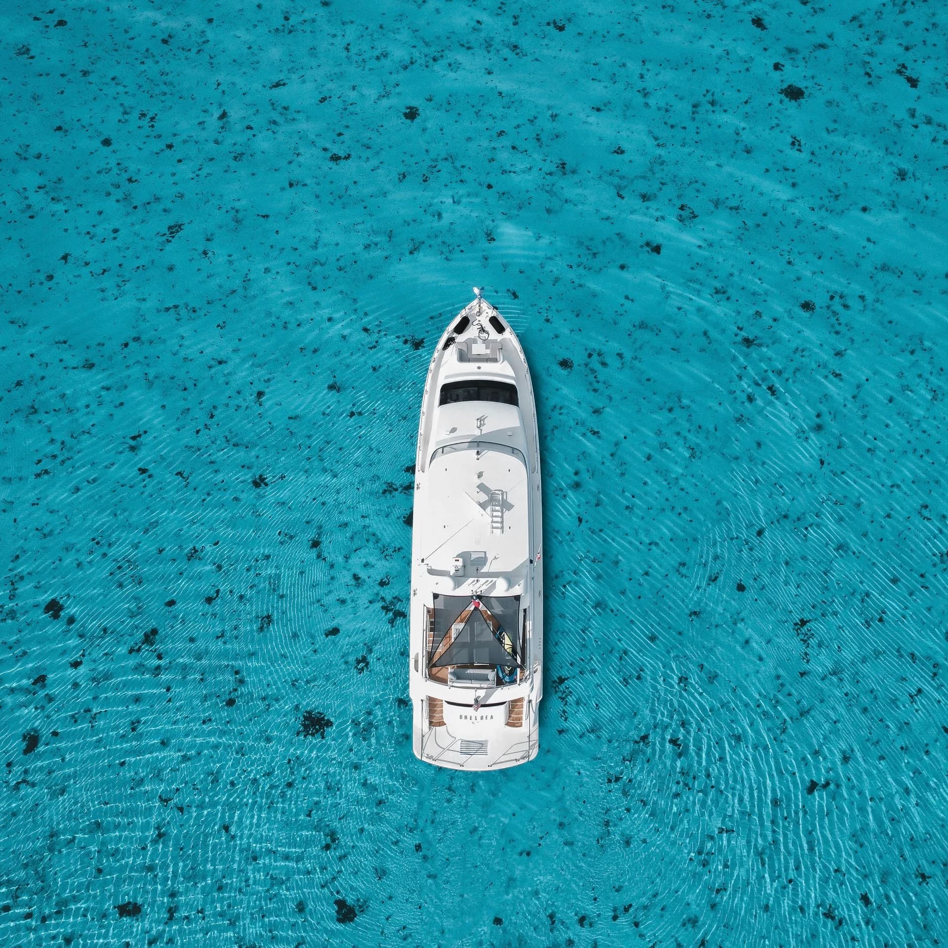 Overhead view of a white motor yacht on turquoise water.