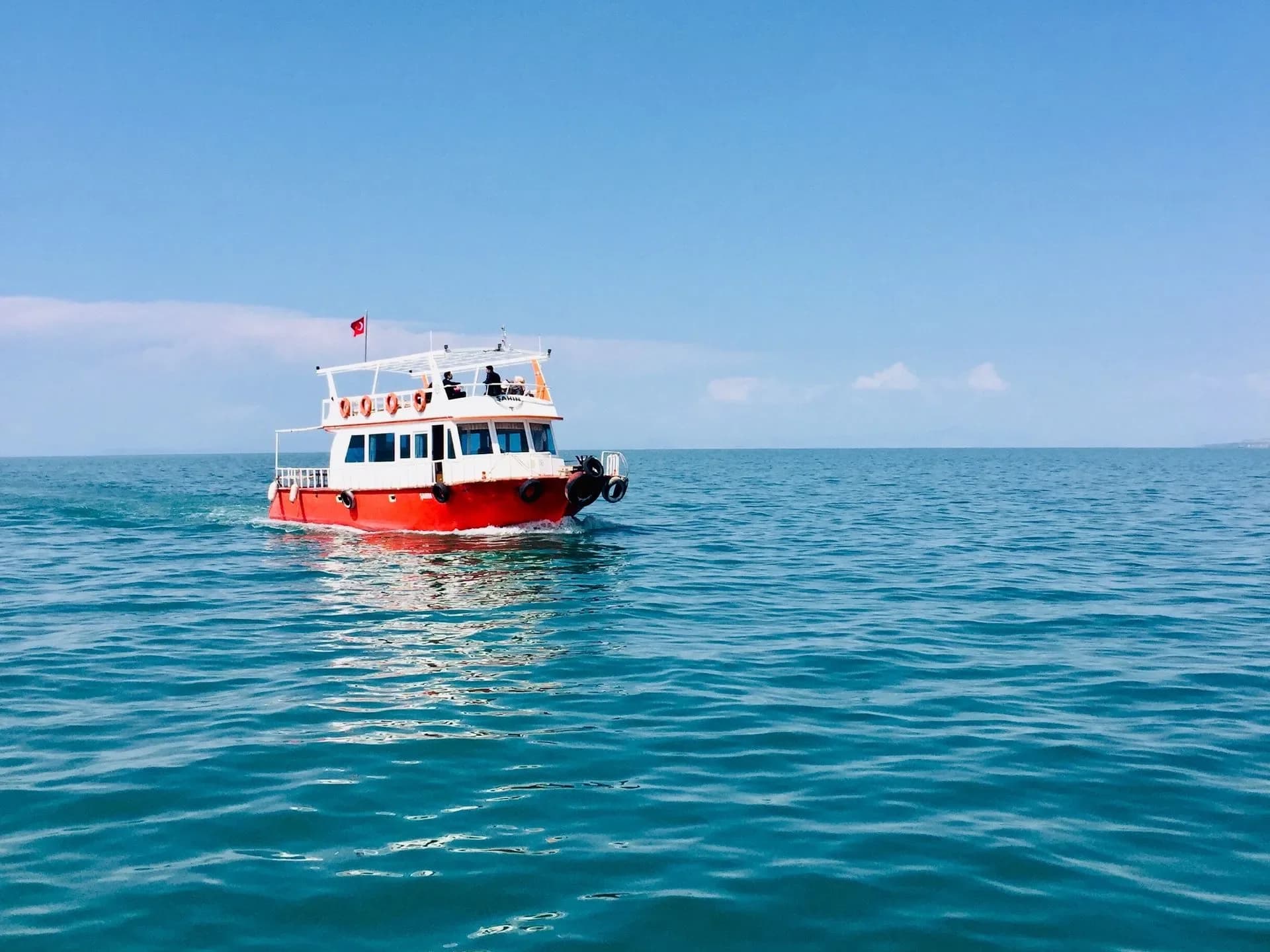 A red motorboat on the sea beneath a blue sky.