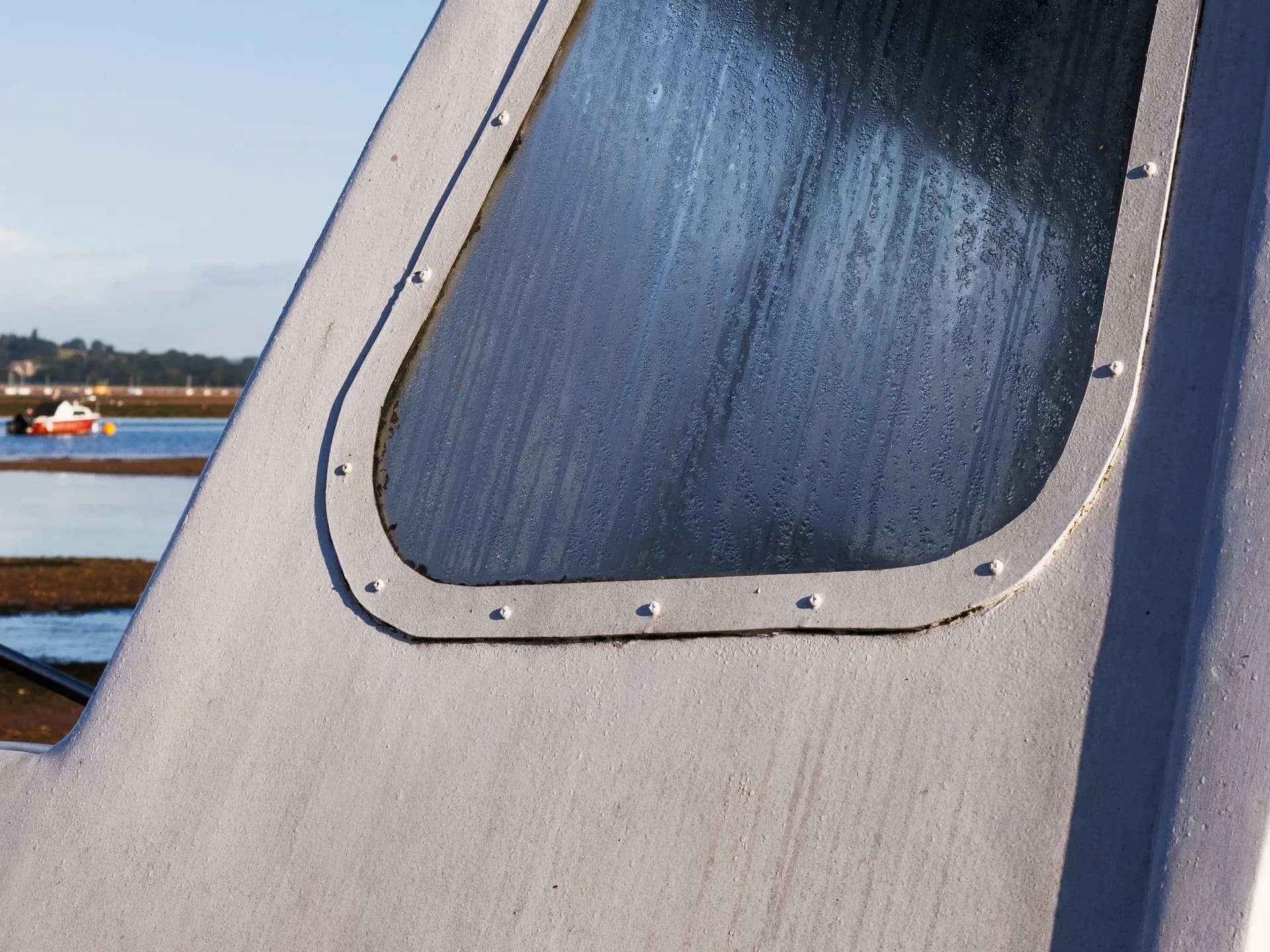 A boat window beside a river under a clear blue sky.