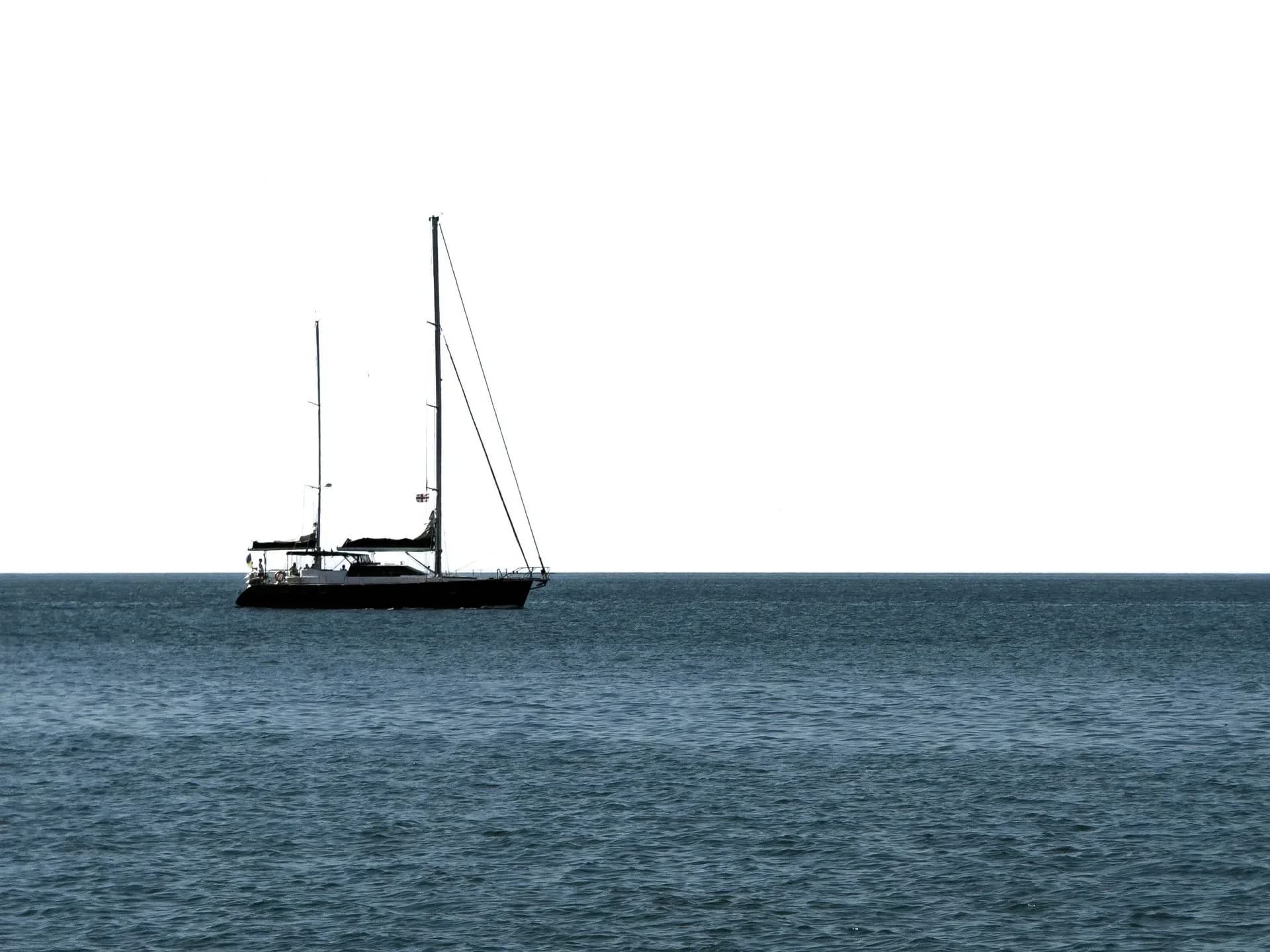 A lone sailboat on calm water beneath a clear sky.