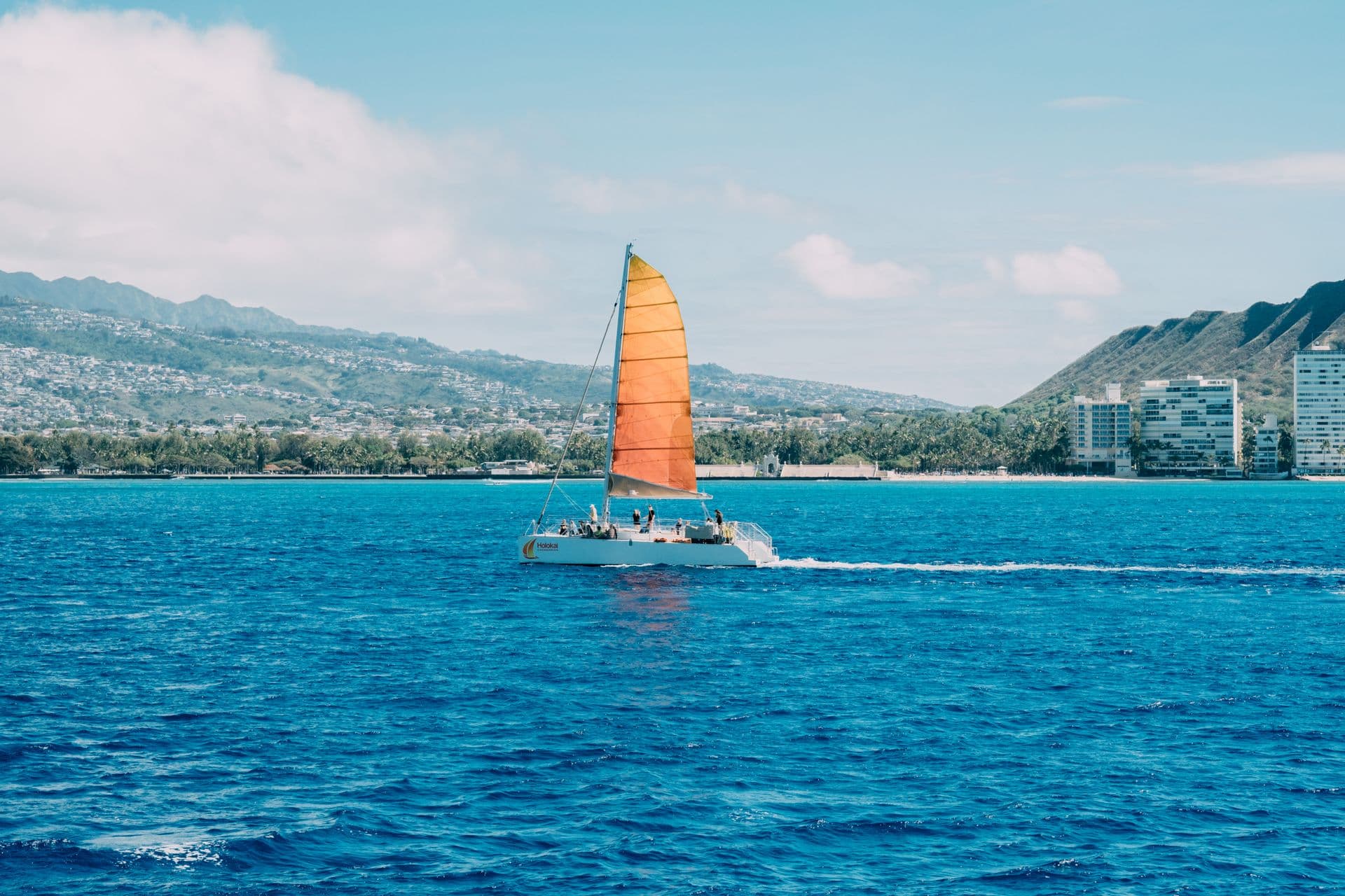 Catamaran with an orange sail sailing near the coast of Honolulu